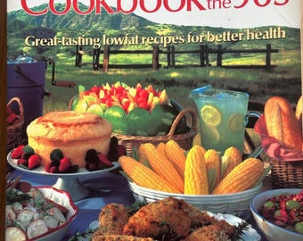 Könnte beinhalten: Ein Kochbuch mit dem Titel Cookbook for the 90s: Great-tasting lowfat recipes for better health von Helen V. Fisher. Das Cover zeigt ein Picknick mit gebratenem Hähnchen, Maiskolben, einem Kuchen mit Beeren, Obstsalat und Limonade.
