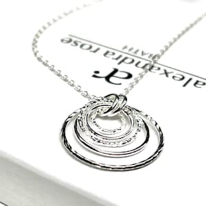 May include: Silver necklace with a pendant of five interlocking circles. The circles are textured and have a hammered finish. The necklace is on a white background with the text "Alexandra Rose" printed on it.