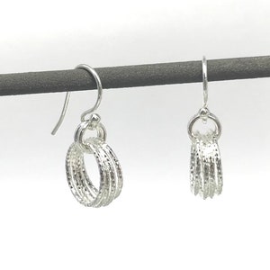 May include: A pair of silver hoop earrings with a textured finish. The earrings are hanging from a black display stand.