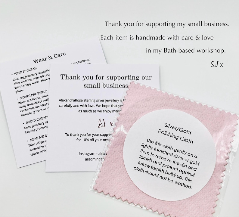 May include: A close-up of a pink polishing cloth for silver and gold jewelry, with a white label. The label provides instructions for use. There are also care instruction cards and a thank you card.