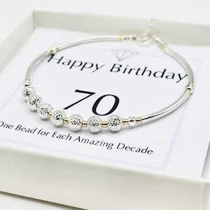 May include: Silver bracelet with faceted beads and gold details, presented in a white gift box. The card reads "Happy Birthday 70" with the text "One Bead for Each Amazing Decade". A perfect gift for a 70th birthday.