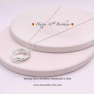 May include: A silver necklace with a pendant made of five interlocking rings. The necklace is displayed on a white surface with the text "Happy 30th Birthday" above it. Sterling Silver jewellery Handmade in Bath www.alexandra-rose.com