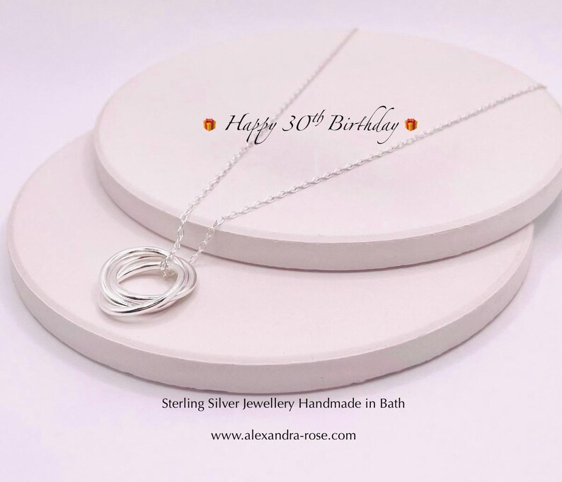 May include: A silver necklace with a pendant made of five interlocking rings. The necklace is displayed on a white surface with the text "Happy 30th Birthday" above it. Sterling Silver jewellery Handmade in Bath www.alexandra-rose.com