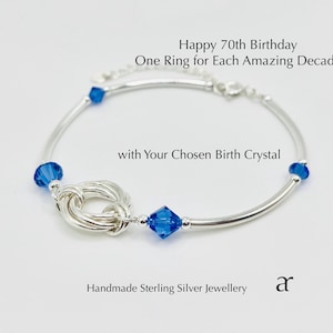 Peut inclure: Un bracelet en argent avec des cristaux bleus. Le bracelet présente un motif de nœud et porte l'inscription : "Happy 70th Birthday, One Ring for Each Amazing Decade, with Your Chosen Birth Crystal."