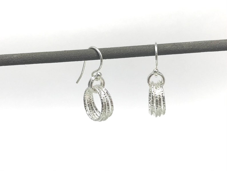 May include: A pair of silver hoop earrings with a textured finish. The earrings are hanging from a black display stand.