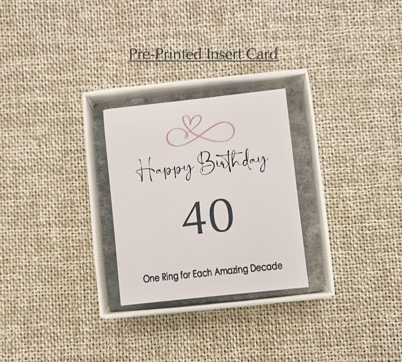 May include: A white card with pink hearts and the text "Happy Birthday 40 One Ring for Each Amazing Decade".