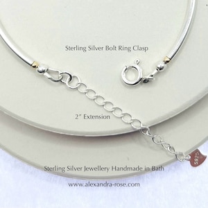 May include: A sterling silver necklace with a bolt ring clasp and a 2-inch extension. The necklace is silver with gold-colored accents. The text "Sterling Silver Bolt Ring Clasp", "2" Extension", and "Sterling Silver Jewellery Handmade in Bath" are visible.
