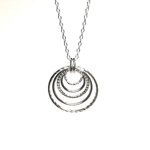May include: A silver necklace with a pendant made of five interlocking circles.