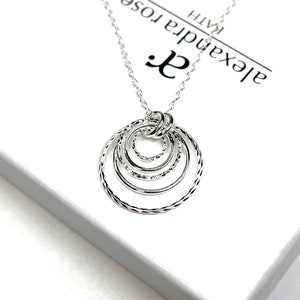 May include: Silver necklace with a pendant of five interlocking circles. The circles are textured and have a delicate, feminine design. The necklace is on a white background with the text "Alexandra Rose Bath" visible.