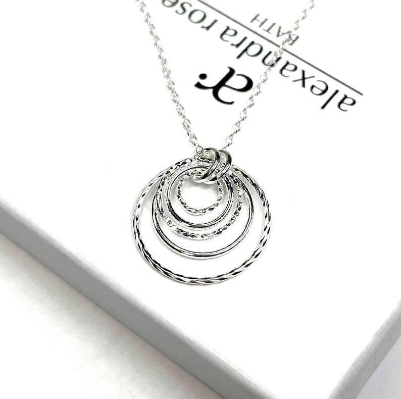 May include: Silver necklace with a pendant of five interlocking circles. The circles are textured and have a delicate, feminine design. The necklace is on a white background with the text "Alexandra Rose Bath" visible.