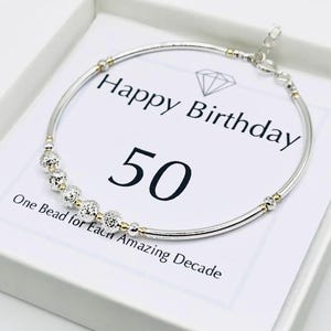 May include: Silver-tone bracelet with gold accents and decorative beads. The bracelet is presented on a white card with the text "Happy Birthday 50" and "One Bead for Each Amazing Decade."