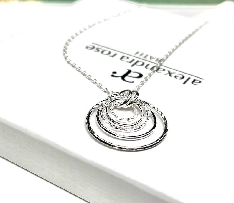 May include: Silver necklace with a pendant of five interlocking circles. The circles are textured and have a hammered finish. The necklace is on a white background with the text "Alexandra Rose" printed on it.