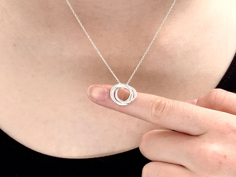 May include: A silver necklace with a pendant made of four interlocking circles.