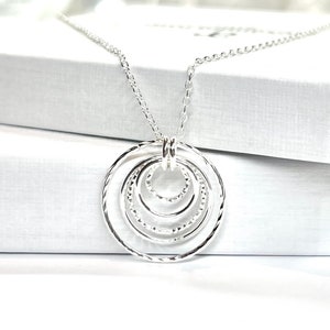 May include: Silver necklace with a pendant featuring five interlocking circles. The circles are textured and have a hammered finish.
