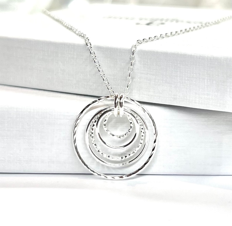 May include: Silver necklace with a pendant featuring five interlocking circles. The circles are textured and have a hammered finish.