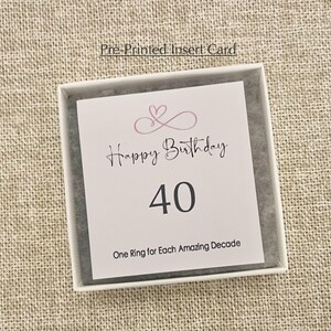 May include: A white card with pink hearts and the text "Happy Birthday 40 One Ring for Each Amazing Decade".