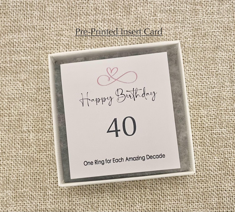 May include: A white card with pink hearts and the text "Happy Birthday 40 One Ring for Each Amazing Decade".
