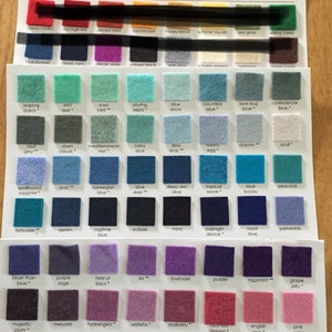 May include: A color chart featuring rows of small square 100% Merino wool felt swatches in various shades. Each swatch is labeled with a specific color name printed in black text below it. The display includes a wide spectrum of colors.