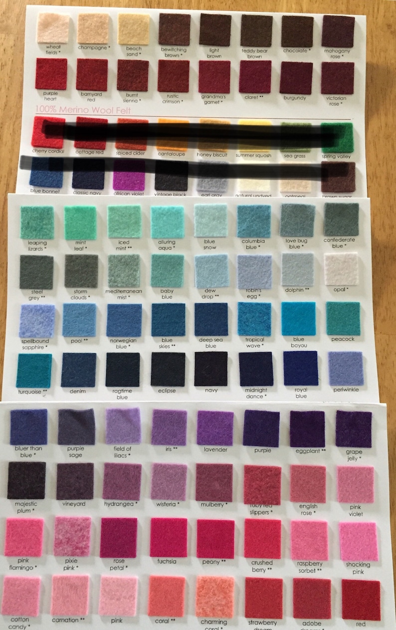 May include: A color chart featuring rows of small square 100% Merino wool felt swatches in various shades. Each swatch is labeled with a specific color name printed in black text below it. The display includes a wide spectrum of colors.