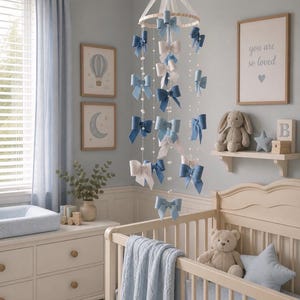 May include: A hanging nursery mobile featuring multiple fabric bows in shades of blue and white, suspended from a circular frame with white ribbons and strings of small white beads, creating a cascading decorative display above a crib.