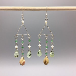 May include: Silver dangle earrings with a triangular design, featuring green and white beads, and teardrop-shaped stones.