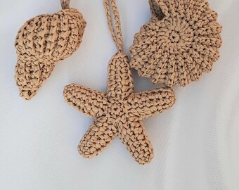 May include: Three woven raffia beach-themed charms. The charms include a seashell, a starfish, and a circular design. Each charm is attached to a gold-colored metal ring. The charms are tan and sit on a white background.