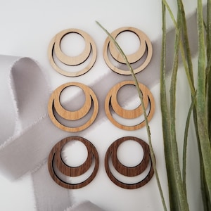 May include: Six wooden earrings in the shape of a crescent moon. Three earrings are made of light wood and three earrings are made of dark wood.
