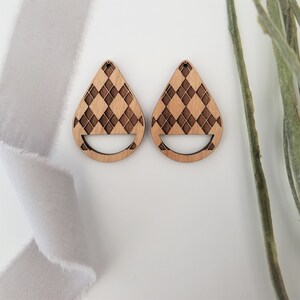 May include: A pair of wooden teardrop-shaped earrings with a checkered pattern. The earrings have a cutout design at the bottom.