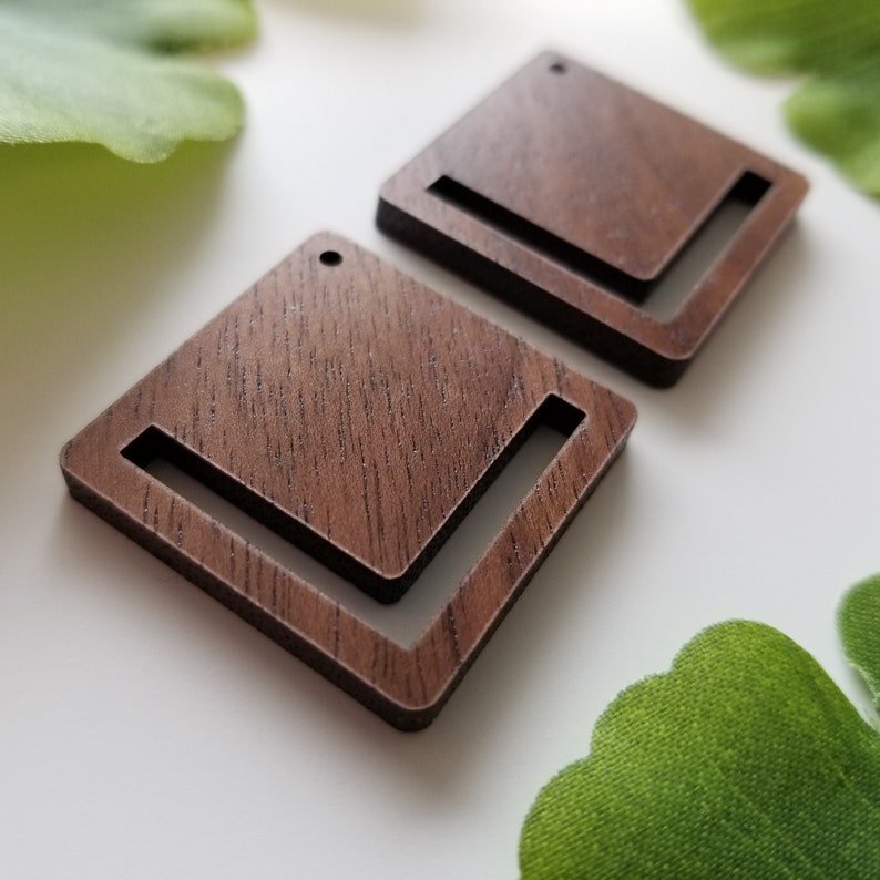 May include: Two square wooden earrings with a cutout in the shape of an L. The earrings are a dark brown colour and have a wood grain texture.