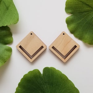 May include: Two unfinished wooden diamond-shaped earrings with a cut-out chevron design. Each earring has a small hole at the top for attaching a hook.