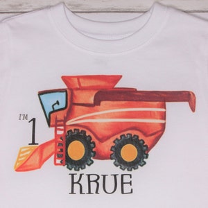 May include: White t-shirt with a red and orange combine harvester graphic. The text "I'm 1" and "KRUE" are printed on the shirt.