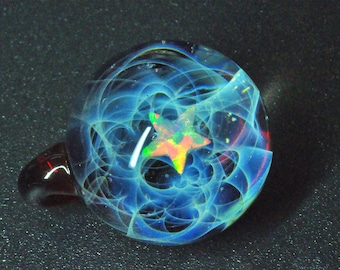 Puede incluir: Un colgante de vidrio con un patrón de remolino azul y blanco y una opala en forma de estrella en el centro.