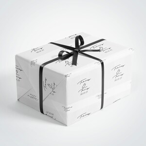 May include: A wrapped gift box with white paper featuring a repeating black script design and the text "Tracey & Terry 30.01.21". The box is tied with a black satin ribbon and bow.
