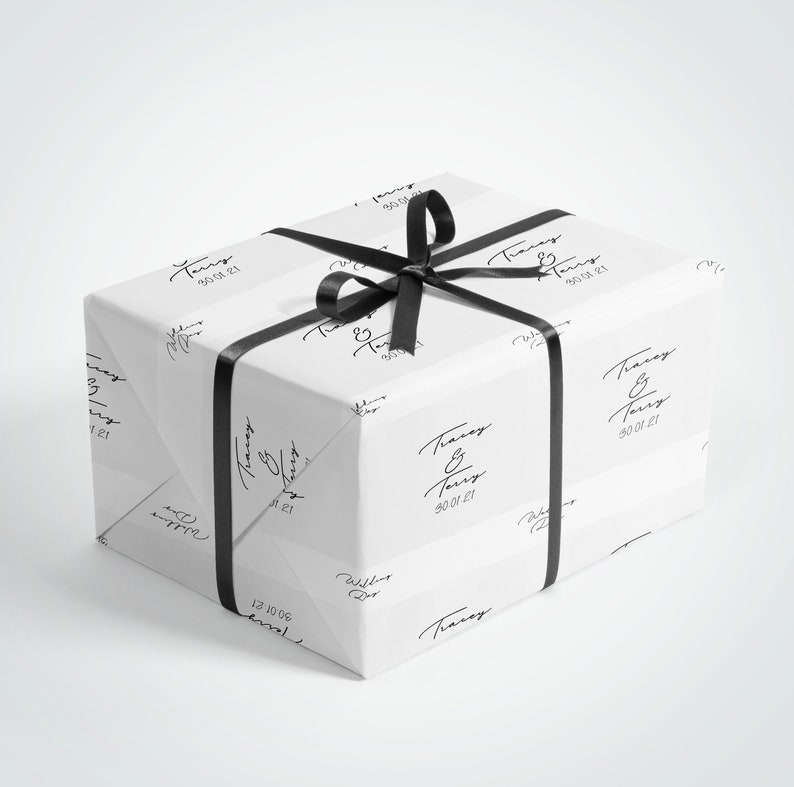May include: A wrapped gift box with white paper featuring a repeating black script design and the text "Tracey & Terry 30.01.21". The box is tied with a black satin ribbon and bow.