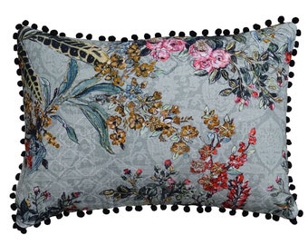 May include: A gray pillow with a floral print and black pom-pom trim. The flowers are in shades of pink, red, yellow, and blue.