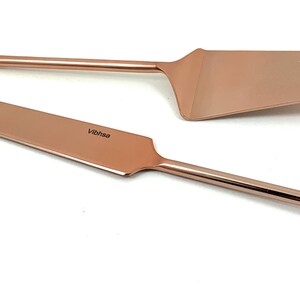 May include: A set of two rose gold cake servers with a spiral design on the handles. The servers are made of stainless steel and have a polished finish.