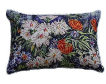 May include: A rectangular pillow with a white pom-pom trim. The pillow features a floral print with white, pink, orange, and green flowers on a dark blue background.