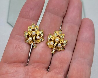 May include: A pair of gold tone earrings with a leaf design and white pearl accents.