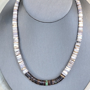 May include: A necklace made of white, brown, and black shell beads with a turquoise accent. The necklace is displayed on a gray mannequin bust.
