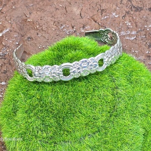 May include: A silver bracelet with a floral design. The bracelet is made of metal and has a delicate, intricate pattern.