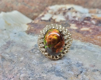 May include: A gold ring with a large, oval-shaped, multi-colored agate gemstone set in a textured, gold setting.