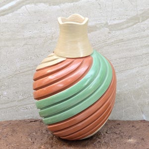 May include: A hand-crafted ceramic vase with a swirl design in shades of green, orange, and cream. The vase has a unique, rounded shape and a textured surface.