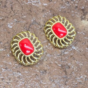 Op de afbeelding: Een paar gouden oorbellen met rode cabochonstenen. De oorbellen hebben een delicaat, versierd ontwerp.