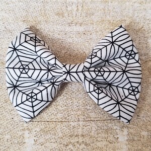 May include: A white bow with a black spiderweb pattern.