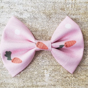 May include: A pink fabric bow with a white polka dot pattern and a carrot print.
