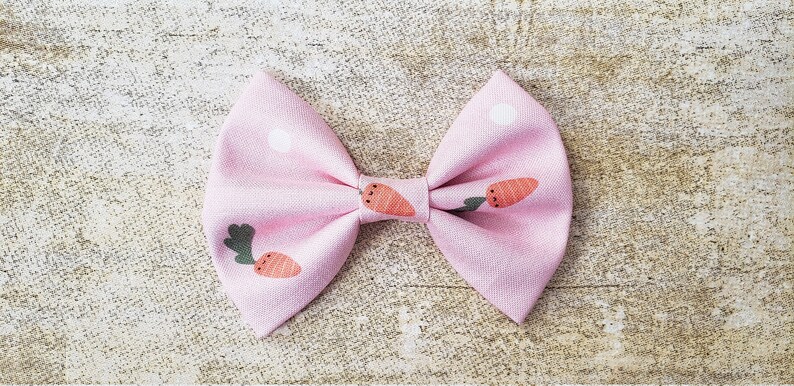 May include: A pink fabric bow with a white polka dot pattern and a carrot print.