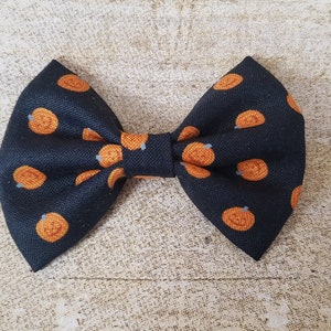 May include: A black bow tie with a pumpkin pattern. The bow tie is made of fabric and has a small loop on the back for attaching it to clothing.
