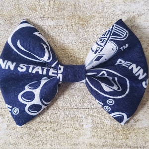 Puede incluir: Una pajarita de tela azul marino y blanca con las palabras "PENN STATE" y el logotipo de la universidad. La pajarita est&aacute; hecha de una tela estampada y est&aacute; atada en el centro.