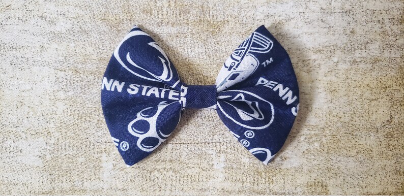 Puede incluir: Una pajarita de tela azul marino y blanca con las palabras "PENN STATE" y el logotipo de la universidad. La pajarita est&aacute; hecha de una tela estampada y est&aacute; atada en el centro.