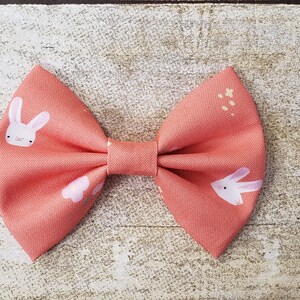 May include: A coral pink bow with a white bunny rabbit print. The bow has a small white center.